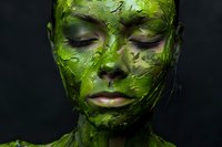 Young woman with closed eyes covered in textured green cosmetic mask against dark background, representing natural skincare and spa treatments.