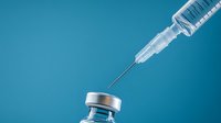 Medical syringe with needle approaching vaccine vial on blue background, minimalist composition showing vaccination and immunization concept.