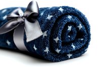 Rolled navy blue plush blanket with white star pattern and silver satin ribbon bow, cozy soft throw for home decor and comfort on white background.