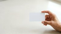 Adult hand holding blank white card against neutral background, suitable for business presentations, marketing mockups, and promotional designs.