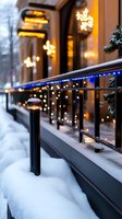 Festive winter street view with illuminated snowflake decorations and blue LED lights along snowy railing, creating warm holiday atmosphere against evening storefront.