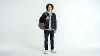 Young man with curly dark hair and light skin tone wearing casual black jacket, carrying brown backpack, standing against white background for lifestyle and fashion design use.