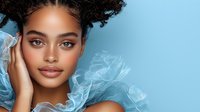 Young African American woman with natural curly hair in space buns style, wearing light blue tulle fabric, on blue background. Glamour beauty portrait with soft makeup.