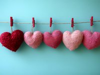 Handmade knitted hearts in pink and red tones hanging on rope with clothespins against turquoise background for Valentine's Day crafts and decor.