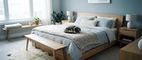 Scandinavian bedroom with wooden bed frame, soft blue bedding, and minimalist decor. Bright natural light from windows illuminates the serene space with potted plants and neutral tones.
