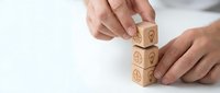 Hands of a Caucasian male stacking wooden cubes with brain and lightbulb icons, symbolizing creativity, innovation, and strategic thinking.