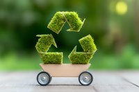 Moss covered recycling symbol on toy wooden cart against green background represents eco-friendly transportation and sustainable delivery solutions.