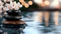 Zen stones pyramid with white orchid flowers on water surface against blurred warm bokeh lights, reflecting peaceful spa atmosphere.