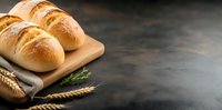 Fresh baked bread rolls on wooden cutting board with wheat ears and linen napkin against dark rustic background with copy space. Food photography.