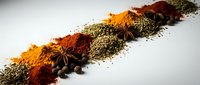 Colorful spices and herbs arranged in diagonal line including turmeric, paprika, star anise, peppercorns and dried seasonings on white background for cooking.
