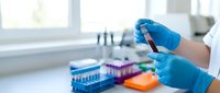 Laboratory technician in blue gloves holding blood sample tube in modern medical lab with colorful test tubes and equipment for clinical analysis.