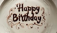 Chocolate text Happy Birthday written in liquid chocolate syrup with decorative swirls on white plate, elegant celebration message for greeting cards and social media.