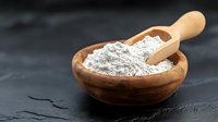 Wooden bowl filled with white flour powder and wooden scoop on dark slate surface for baking and cooking ingredients in rustic kitchen setting.