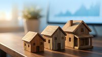 Three wooden miniature house models on a desk with a blurred chart screen background, symbolizing real estate investment and property market growth.