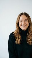 Happy young Caucasian woman with long wavy brown hair wearing black turtleneck sweater smiling at camera against white background for lifestyle content.