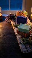 Handmade natural soap bars with herbs and lavender on rustic wooden board in candlelit spa setting for relaxation and skincare routine.