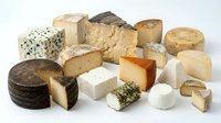 Assorted artisanal cheese varieties including aged cheddar, soft brie, blue cheese, and gouda blocks arranged on white background for culinary and food styling projects.