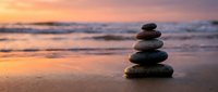 Zen stone stack on beach sand at sunset with ocean waves creating peaceful meditation and balance concept for wellness and mindfulness practices.