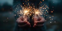 Hands holding bright sparklers creating magical golden sparks against dark background for celebration and festive occasions.