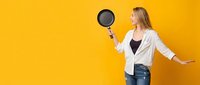 Young blonde woman in white blazer holding frying pan on bright yellow background with copy space for cooking and kitchen advertising concepts.