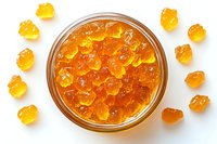 Golden gummy bears scattered around glass jar filled with orange and yellow jelly candies on white background, top view composition for food packaging.