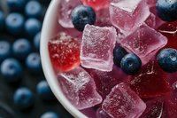 Fresh blueberries and pink jelly cubes dusted with sugar crystals in white ceramic bowl, macro food photography showing texture and sparkle details.