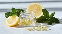 Fresh lemon slices with mint leaves and vitamin capsules on white marble surface, natural health supplement concept.