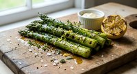 Grilled asparagus spears with herbs and lemon on wooden cutting board. Fresh green vegetables seasoned with thyme, ready for healthy dining and cooking.