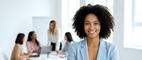 Professional African American businesswoman smiling confidently in modern office with diverse team meeting in background for corporate presentations.