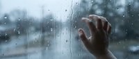 Hand pressed against rain-covered window glass with water droplets, creating melancholic atmosphere for emotional storytelling and mental health concepts.