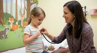 Female pediatrician examining young blonde girl with stethoscope in colorful medical office. Healthcare professional and child patient interaction.