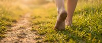 Barefoot person walking on grassy path during golden hour, ideal for wellness, nature, and lifestyle content depicting outdoor relaxation and connection with earth.