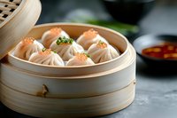Steamed dumplings with delicate pleated wrappers in traditional bamboo steamer, garnished with fresh herbs and sesame seeds, served with dipping sauce.