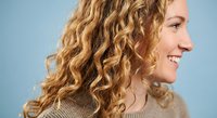Happy Caucasian woman with curly blonde hair smiling in profile against blue background. Natural beauty portrait for lifestyle and wellness content.