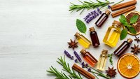 Essential oils in amber bottles with fresh herbs, spices and citrus slices on white wooden background. Natural aromatherapy and wellness concept for spa treatments.