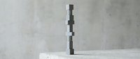 Stack of balanced concrete blocks creating minimalist sculptural tower on white surface against textured gray wall for modern interior design concepts.