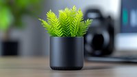 Artificial fern plant in modern black cylindrical pot on desk with blurred office background, minimalist workspace decor with selective focus.