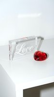 Acrylic block engraved with Love script beside a red glass heart on a white surface, evoking romance for Valentine's Day decor.