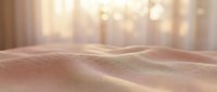 Smooth golden sand dunes with warm sunlight creating soft shadows and highlights, desert landscape with bokeh light effects in background.
