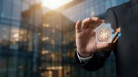 Businessman hand holding transparent percentage symbol with modern office building background representing financial growth and interest rates.