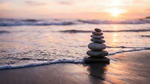 Balanced stone stack on beach at sunset with gentle waves and golden light reflecting on wet sand creating peaceful meditation scene for wellness concepts.