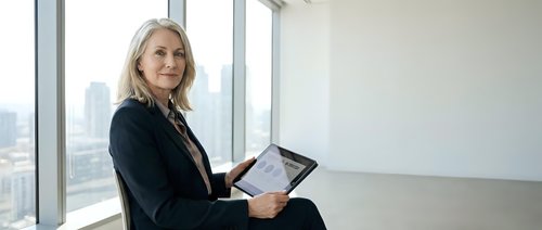Confident mature businesswoman with tablet in modern office space with city view. Professional executive planning strategy and reviewing data.