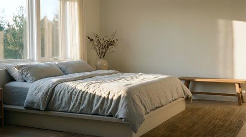 Serene bedroom interior with natural light from large window, neutral tones, minimalist decor, and cozy bedding arrangement for home design and lifestyle content.