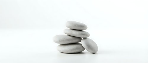 Stacked smooth gray stones balanced on white background, symbolizing zen, meditation, wellness, spa therapy, and mindfulness practices.