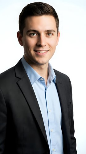Professional young Caucasian businessman in dark suit and light blue shirt smiling confidently on white background isolated for corporate design.