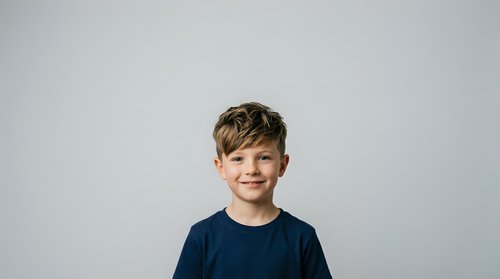 Young boy with light brown hair and fair complexion, wearing a dark navy t-shirt, smiling at camera against neutral gray background. Portrait suitable for family, education, healthcare and lifestyle marketing.