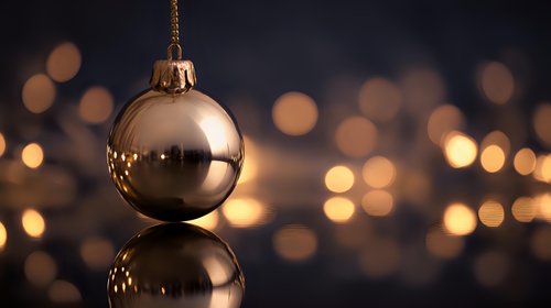 Elegant gold Christmas ornament with reflection against dark background with warm bokeh lights for holiday decoration.
