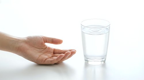 Young adult hand reaching toward glass of fresh water on white surface, isolated on white background for healthcare, wellness, hydration, and medical design use.