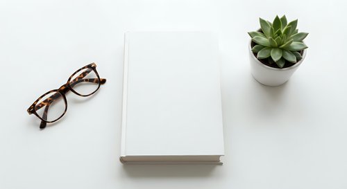 Minimalist workspace with blank notebook, eyeglasses and succulent plant on white desk. Clean office setup for productivity and planning.