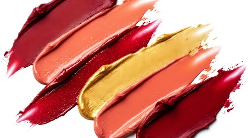 Colorful lipstick smears in warm autumn tones including burgundy coral gold and red creating artistic makeup swatches on white background for beauty cosmetics.